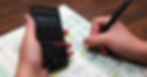 A person sitting at their desk using a pen and calculator to keep track of financial information for recordkeeping.