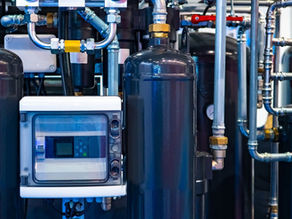 A group of black compressed air tanks standing upright. They have shiny aluminum pipes and gauges coming out from the top.