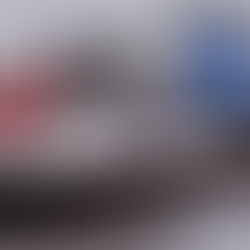 Two jet skis, one blue and one red, are tied to a wooden dock on a calm lake on a dreary day, ready to ride.