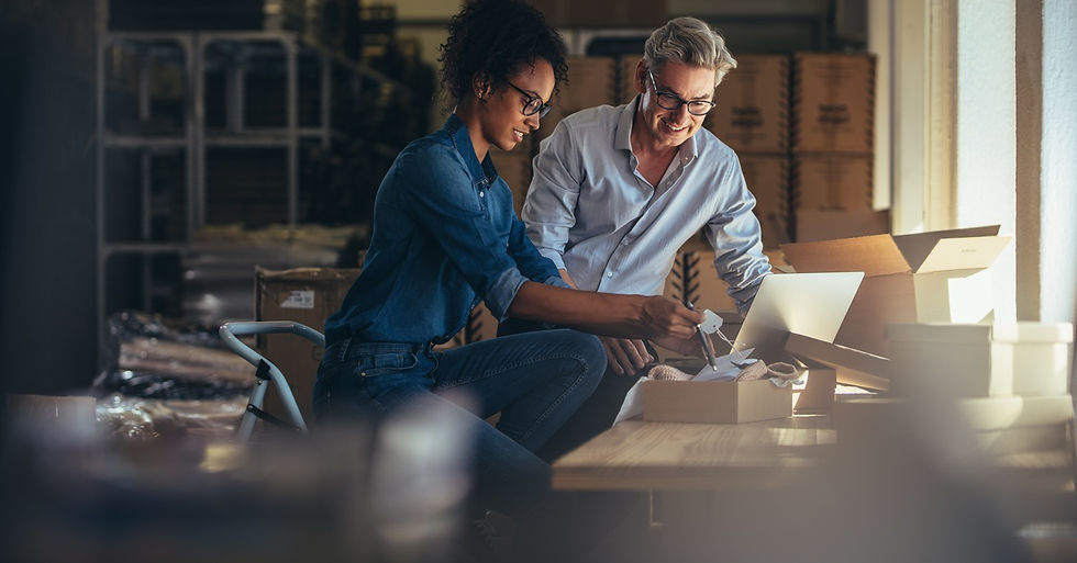 A man and a woman sitting next to one another in their store while packing products to be delivered to customers.