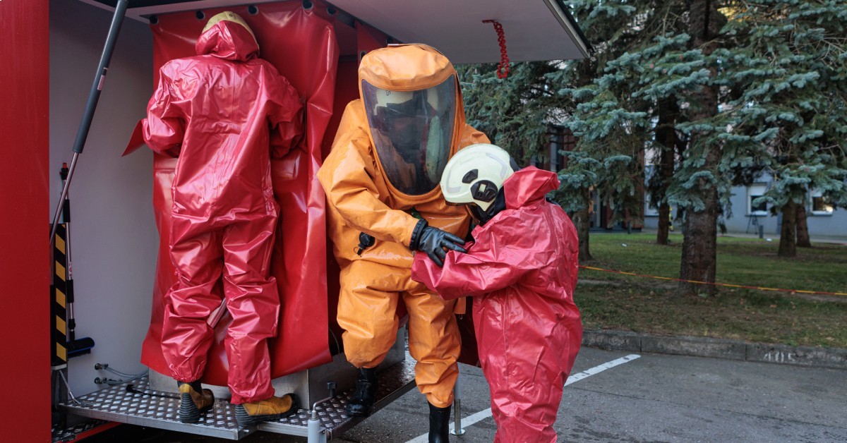 A group of people are all in protective hazmat suits. Two suits are red while the third one is orange.