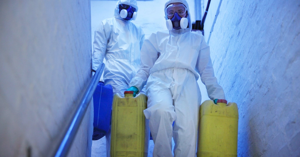Two people, both in protective equipment, are walking down a stairwell. They’re each holding containers.