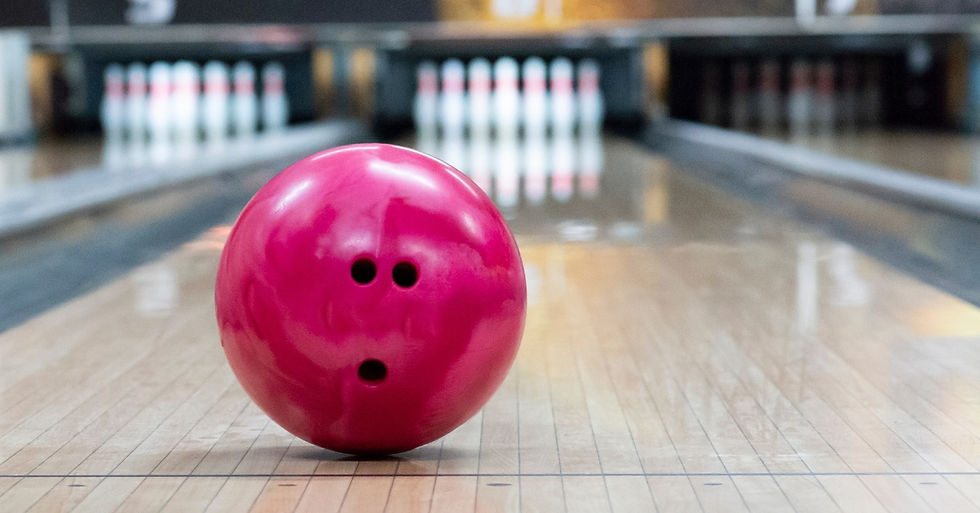 A close-up of a pink bowling ball with the finger holes facing the camera as it rolls down a bowling lane.