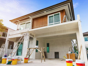 A new house under construction and being prepared for paint. There are ladders and buckets of paint on the ground.