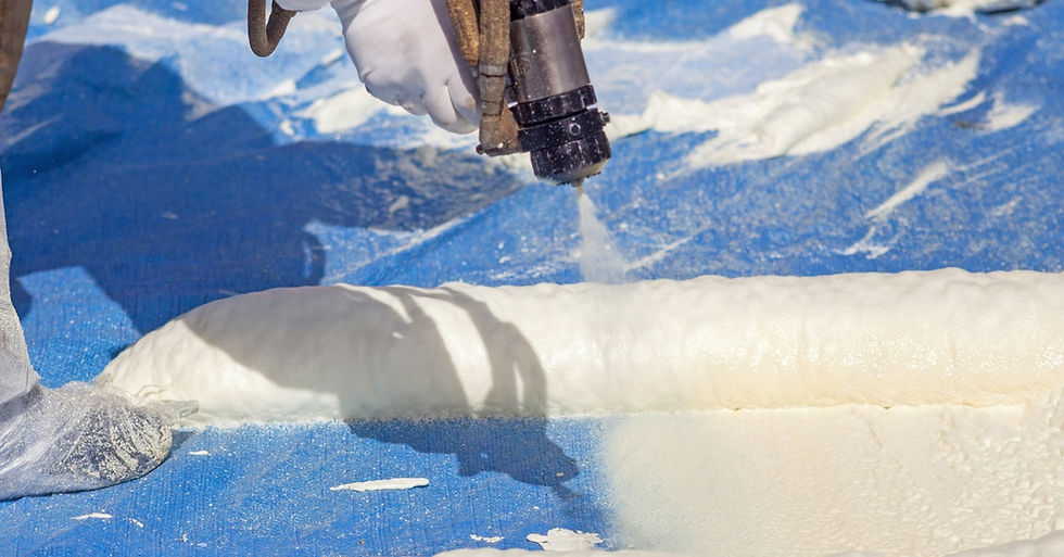 A person wearing a protective suit and gloves standing on a roof while using a spray gun to apply foam insulation.