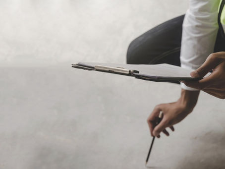 A man is holding a clipboard in one hand and a pencil in the other. He’s looking at the clipboard while kneeling.