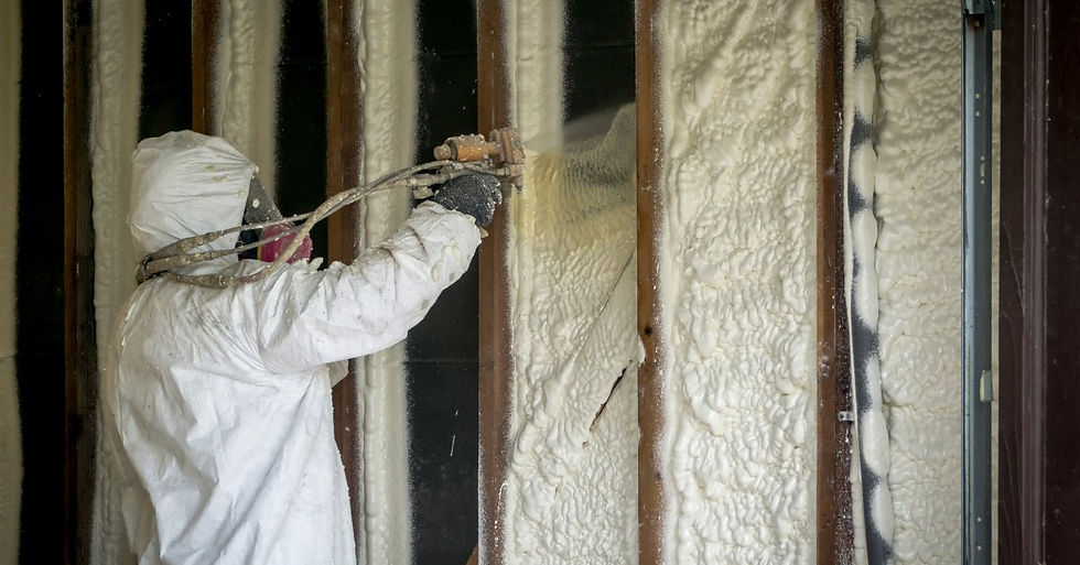 A person wearing a full-body protective suit and holding a hose to spray closed-cell insulation into the wall.
