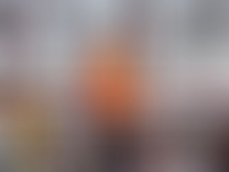 An older man looks at a tablet while standing on an elevated platform at an industrial plant, a maze of silver piping behind him.