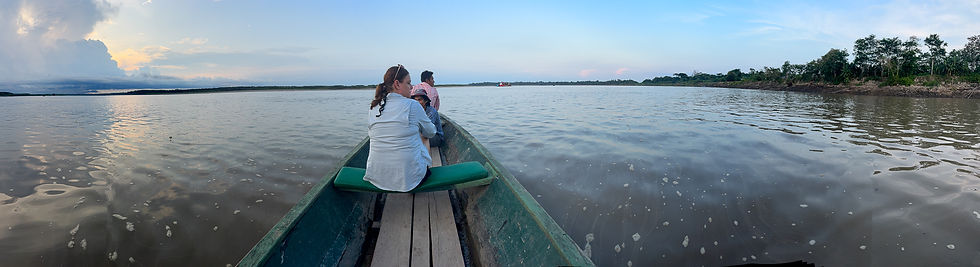 Three people in a boat on a calm river, with trees along the shore. The sky is blue with clouds, creating a serene and peaceful mood.