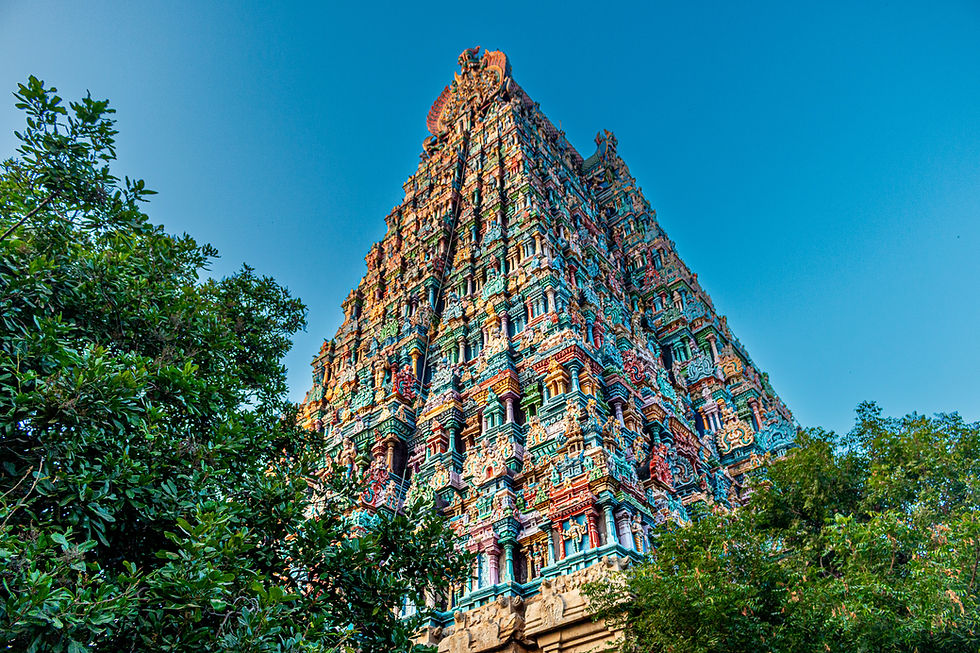 Colorful temple tower adorned with intricate carvings, surrounded by greenery under a clear blue sky, creating a serene atmosphere.