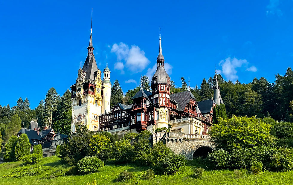 Historic castle with pointed towers and intricate details, surrounded by lush greenery and forest. Blue sky with scattered clouds above.