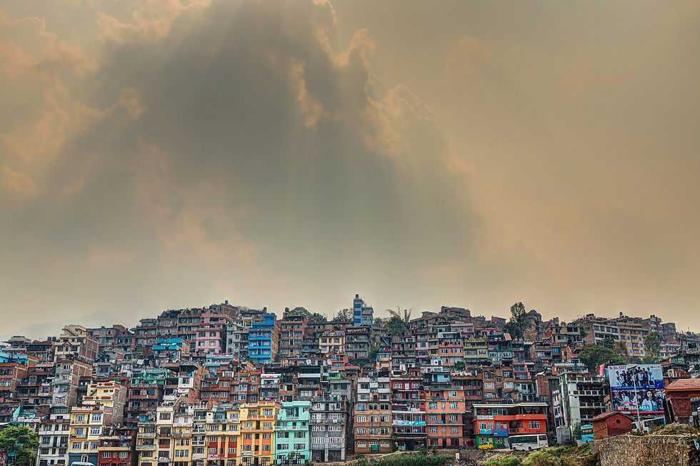 Colorful hillside houses under dramatic, cloudy sky with sunrays. Urban setting with varied architecture creates a vibrant scene.