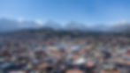 Aerial view of a city with colorful rooftops, set against a backdrop of majestic, snow-capped mountains under a clear blue sky.