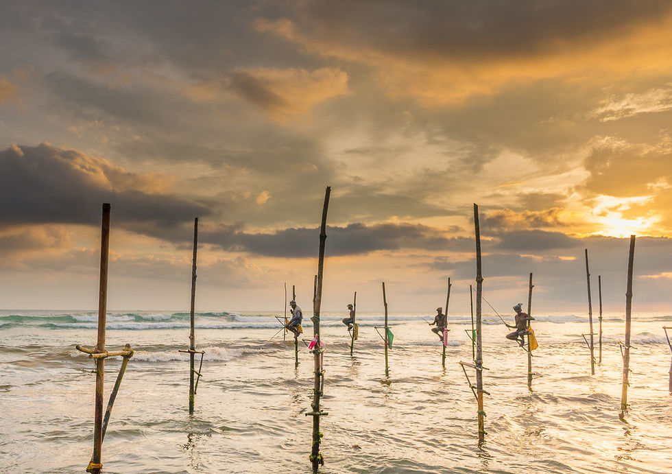 Fishermen on stilts in the ocean at sunset, with dramatic clouds and golden hues creating a serene, picturesque scene.