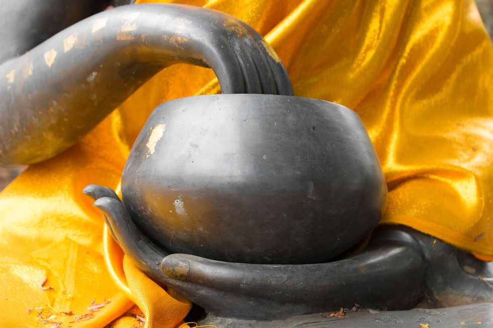 Close-up of a Buddha statue's hands holding a bowl, draped in vibrant orange fabric. Peaceful, serene mood with no visible text.
