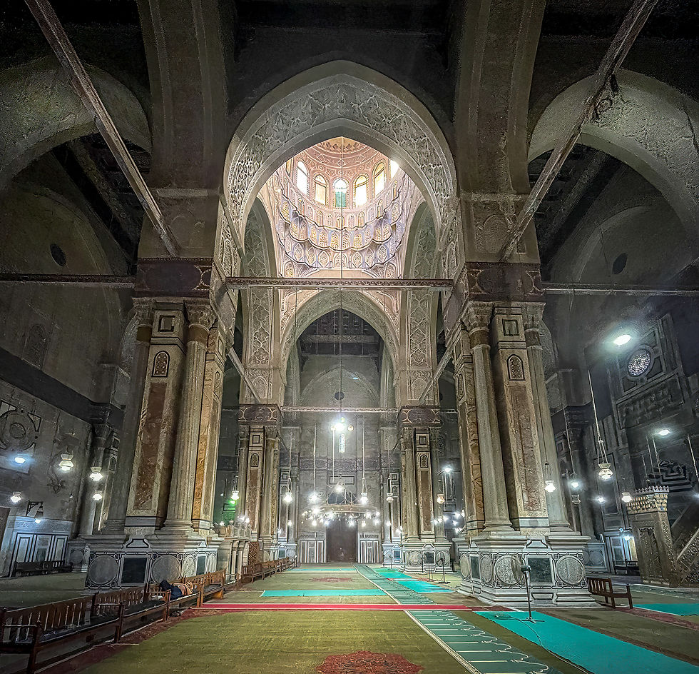 Ornate mosque interior featuring tall arches and intricate patterns. Soft lighting illuminates colorful carpets and creates a serene ambiance.