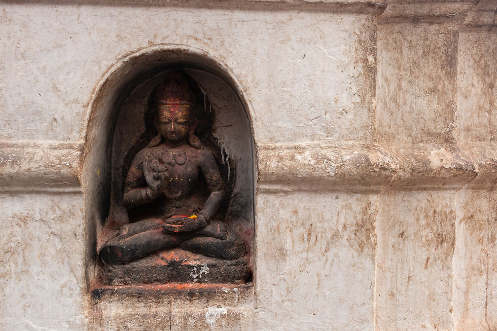 A weathered stone sculpture of a seated deity in a niche, with a calm expression. The background is a textured wall with earthy tones.