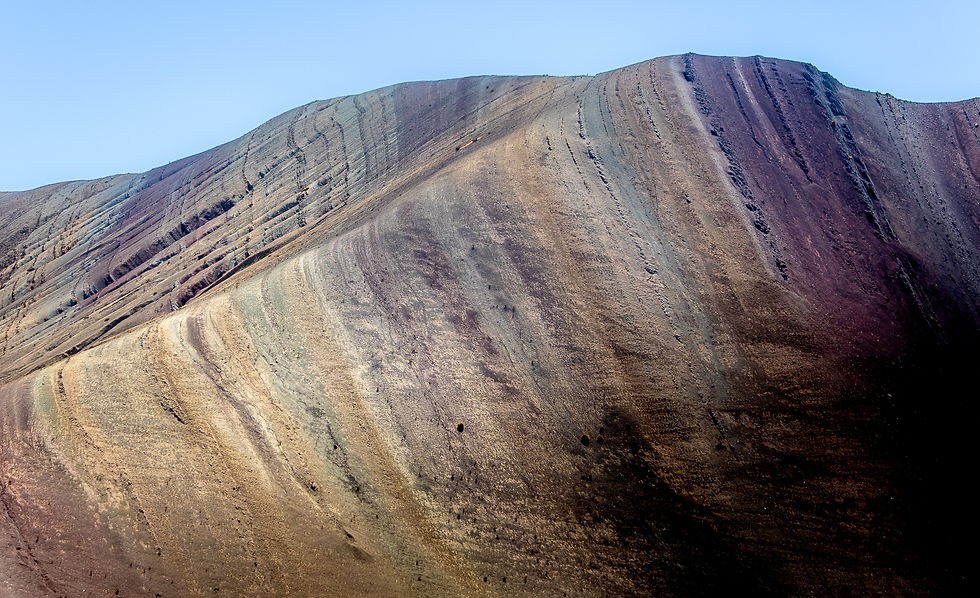 Colorful layered mountain slope under clear blue sky, showcasing earthy tones and distinct texture, evokes a serene natural landscape.