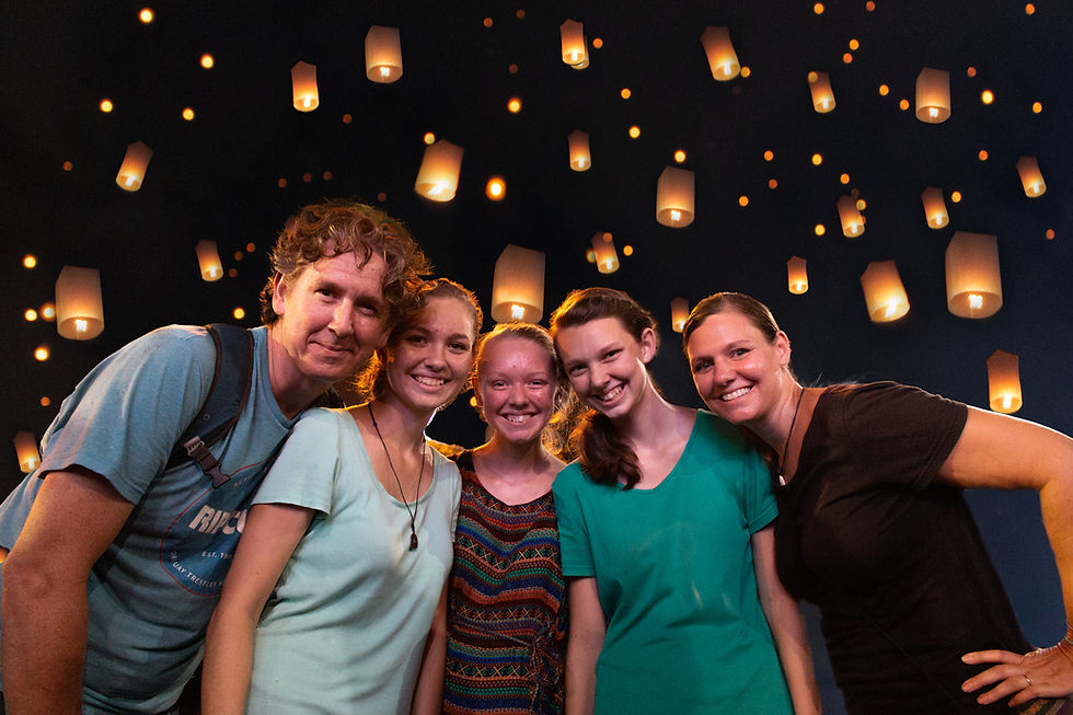 Smiling group posing under a night sky filled with glowing lanterns. They wear casual clothes in a festive atmosphere.