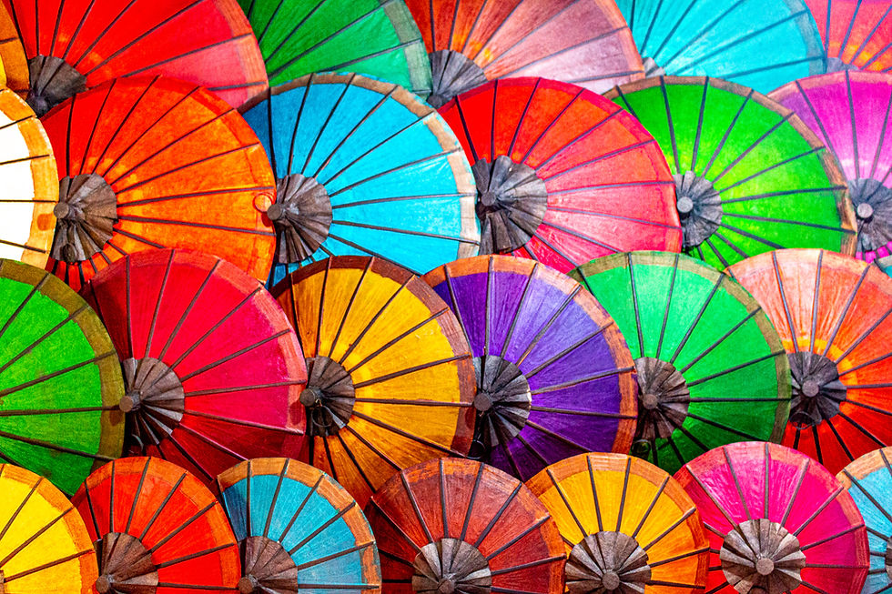 Colorful paper umbrellas overlap, showcasing vibrant reds, blues, greens, and yellows. The mood is lively and festive.