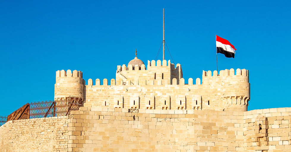 Historic fortress with beige stone walls under a clear blue sky. An Egyptian flag waves atop the battlements. Peaceful and majestic.