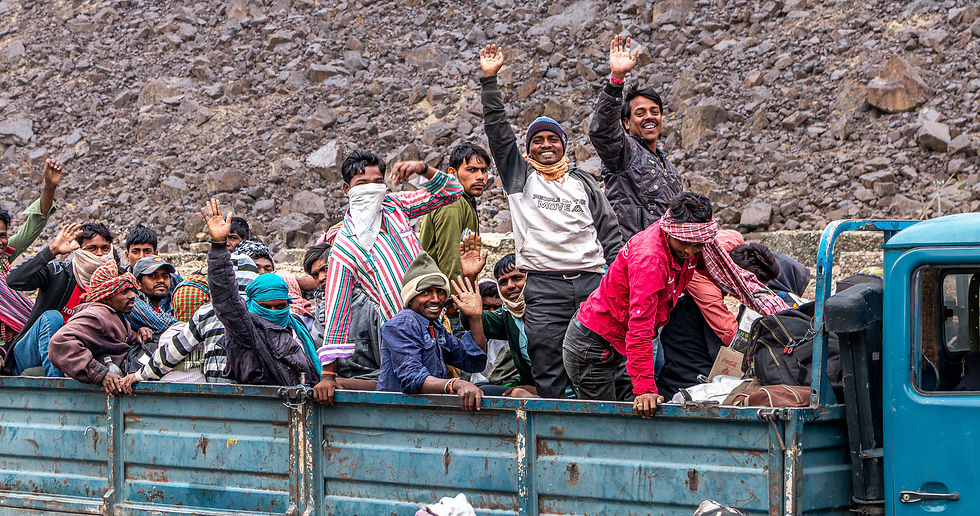 People in colorful attire smile and wave from a blue truck against a rocky background, conveying joy and camaraderie.