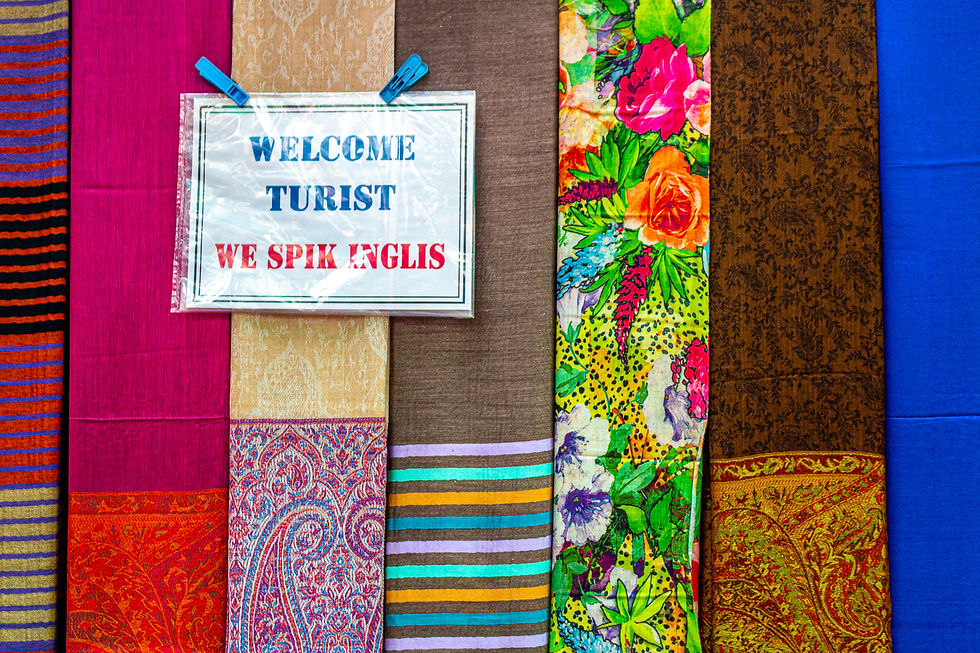 Colorful fabric display with a sign reading "WELCOME TURIST WE SPIK ENGLIS," featuring floral, striped, and paisley patterns, set against a vibrant backdrop.