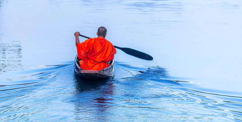 A person in an orange robe paddles a wooden boat across a calm, blue water surface, creating gentle ripples, serene and peaceful setting.