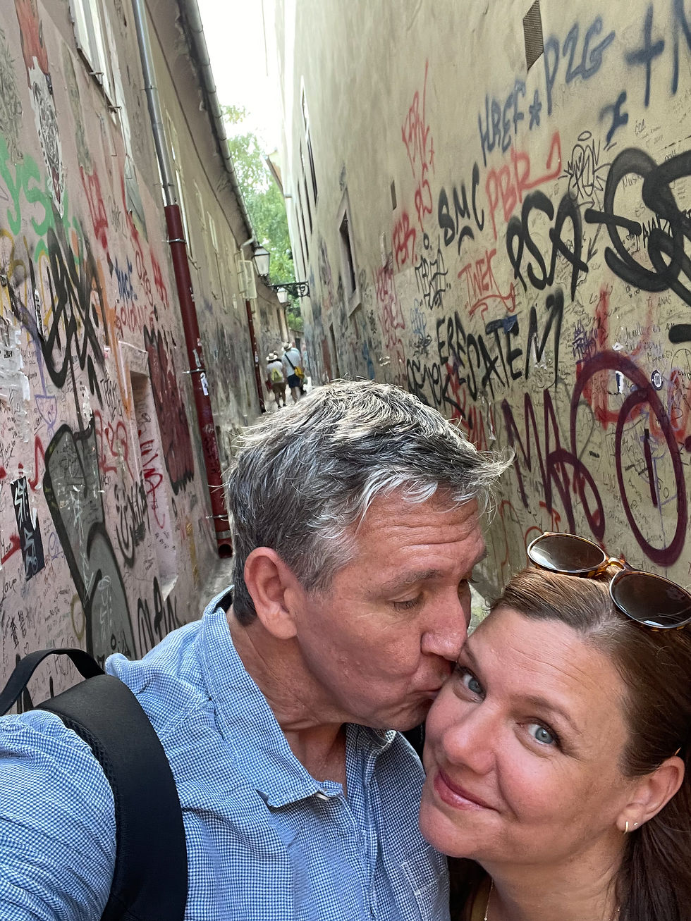 Man kisses woman's cheek in narrow alley covered in colorful graffiti. Both are smiling, creating a joyful mood.