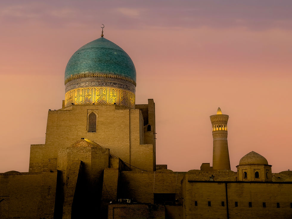 A large turquoise dome and ornate minaret at sunset in a historic cityscape, with a warm pink and orange sky in the background.