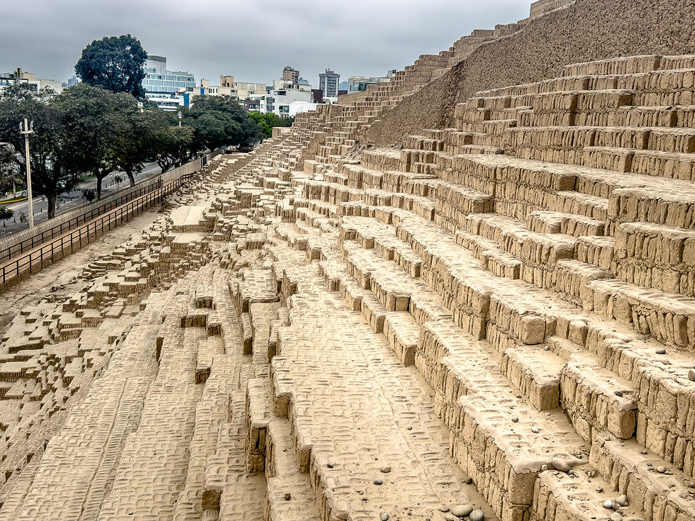 Ancient stepped pyramid made of adobe bricks in an urban area, with trees and buildings in the background under a cloudy sky.