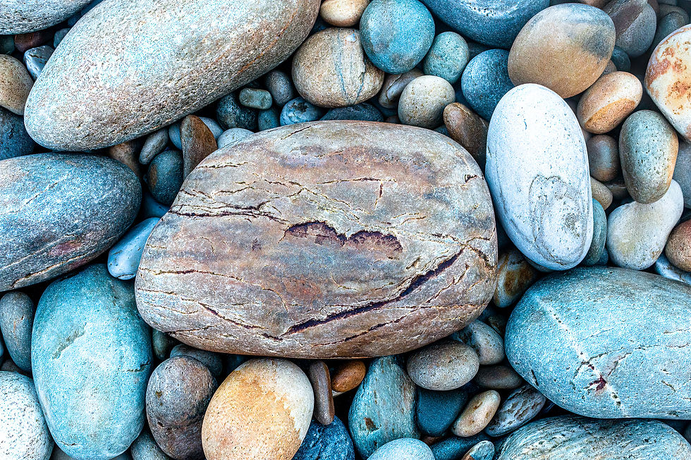 Smooth, multicolored stones in varying sizes fill the frame. Earthy blues, browns, and grays create a tranquil, natural composition.