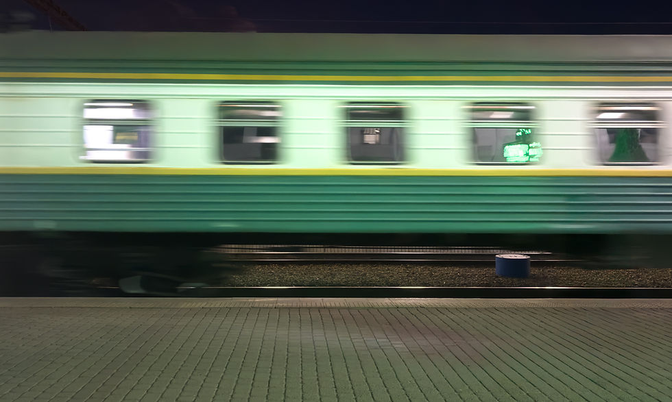 Blurred green and yellow train speeds past on a station platform at night; neon sign visible, creating a dynamic and vibrant scene.