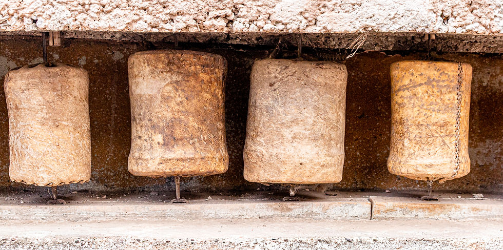 Four rustic, weathered cowbells hang in a row against a textured, earthy background. Brown and beige tones dominate the image.