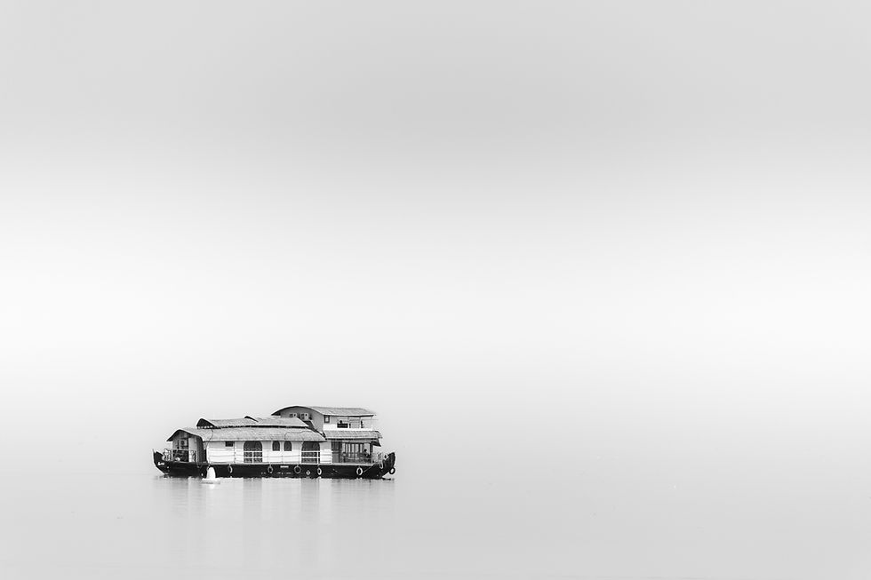 A lone houseboat floats on calm water against a minimalist, gray sky. The scene is peaceful and serene, with no visible text.