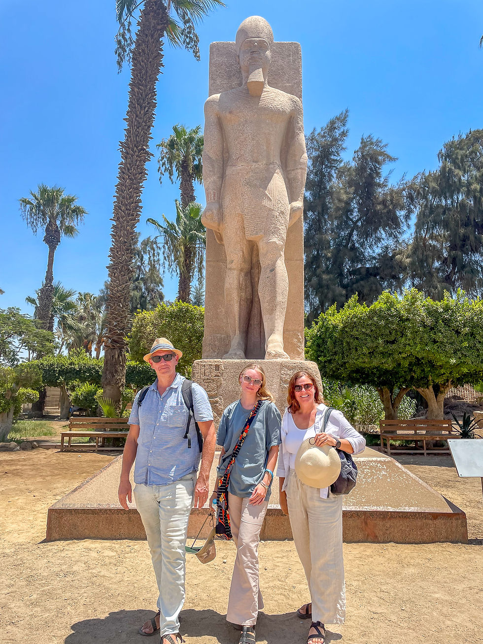 A man, woman, and young woman pose playfully in front of a colossal statue of Ramesses II in Memphis, each mimicking the ancient contrapposto stance with one foot forward.