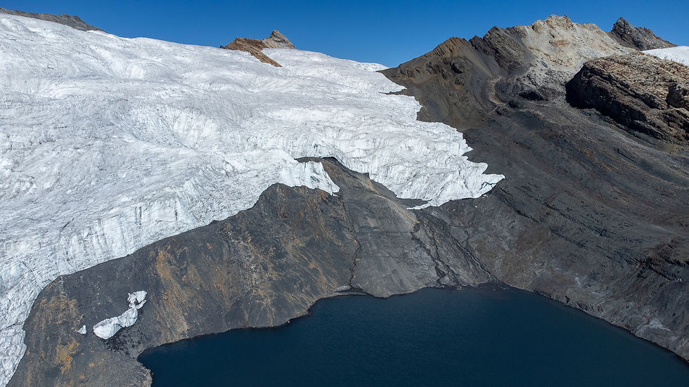 Aerial view of a glacier atop rocky mountain, with blue lake at base. Clear sky and contrasting white ice on dark brown terrain.