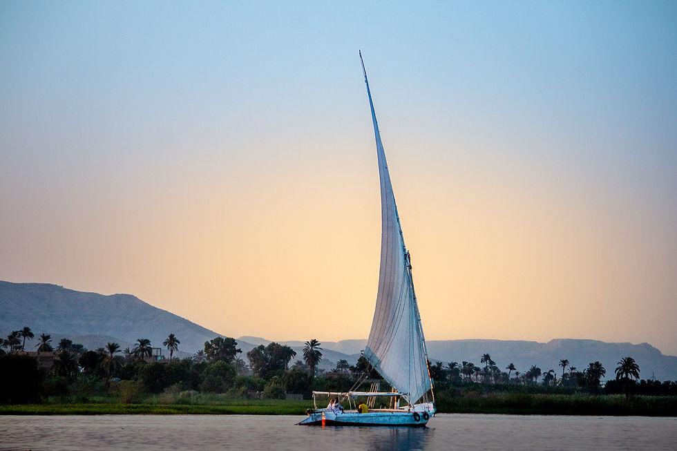 Sailboat with tall mast on calm water at sunset, palm trees and mountains in the background, creating a serene atmosphere.