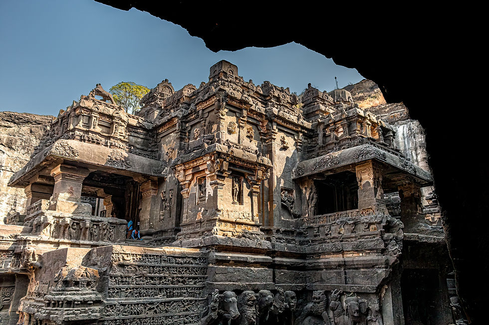 Ancient stone temple with intricate carvings under a clear blue sky. Two people in colorful clothing explore, adding a sense of scale.