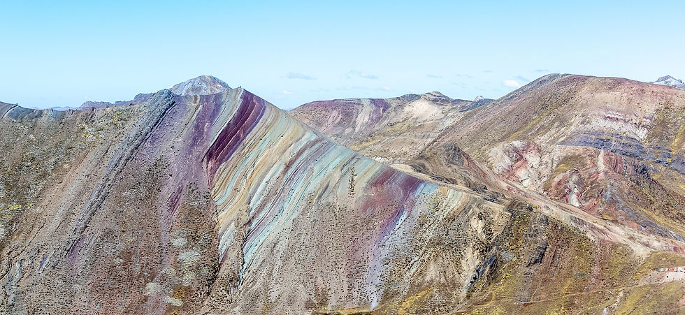 Colorful mountain range with vibrant stripes of purple, red, and turquoise under a clear blue sky, creating a serene and vivid landscape.