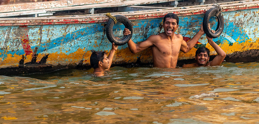 Three men in water, smiling and holding onto tire rings attached to a colorful, worn boat. The mood is joyful and playful.