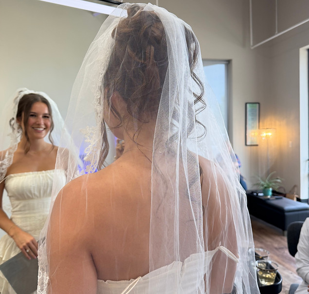 Bride wearing a veil admiring her finished wedding hairstyle in the mirror.