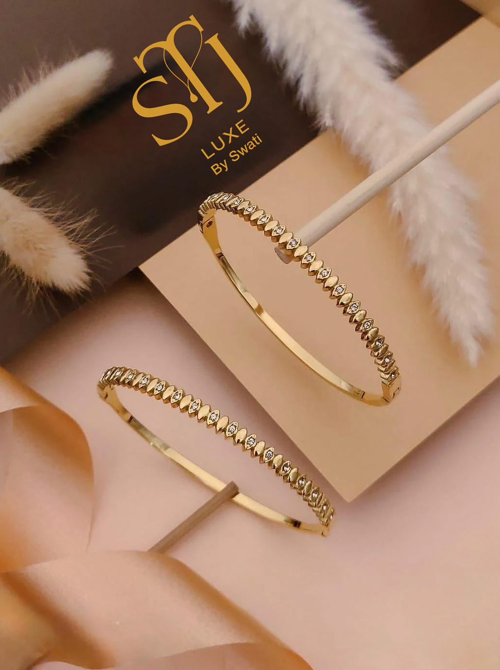 Two sparkling gold bangles on a light pink surface