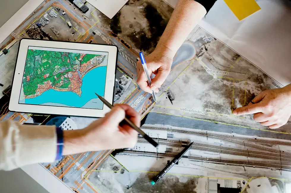 Técnicos analisam mapas digitais e fotografias aéreas sobre uma mesa, com um tablet a mostrar dados geográficos da solução de Gestão Urbanística do City as a Platform.