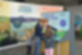Snapshot of the Rivers Alive! exhibit at the independence seaport museum featuring a white woman and two young children in front of the Water Goes Round & Round exhibit.