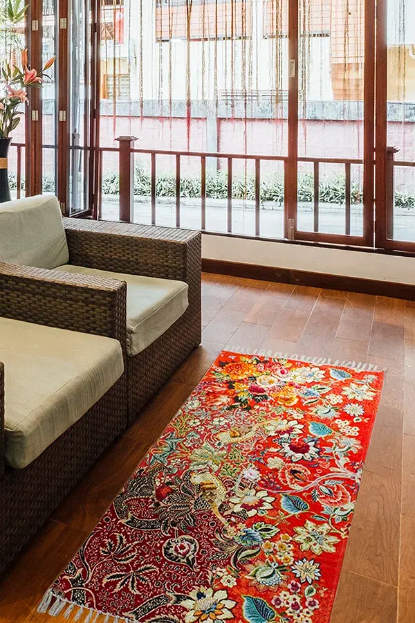 Wicker sofa and vibrant floral rug on a wooden floor in a sunlit room with glass doors. Outdoor plants visible through the windows. Photo Studio in Delhi NCR, amazon Photoshoot, product photography near me, product photoshoot near me, e commerce photoshoot near me