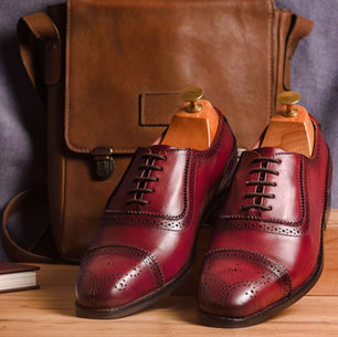 Maroon leather dress shoes with shoe trees next to a brown leather bag on a wooden surface, showcasing professional Amazon product photography and ecommerce photography in Delhi. Perfect example of high-quality Amazon listing photos and Amazon seller photos from a top Amazon product photo studio.