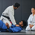 A black belt instructor teaching a Brazilian Jiu-Jitsu technique to a female student in a gi at Agora BJJ academy