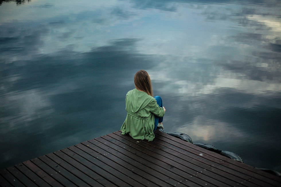 Woman on dock, looking over water reflecting grey skies.