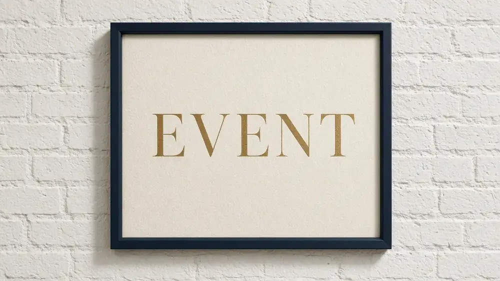 Framed navy and gold 'Event' poster on a white brick wall